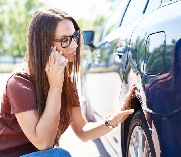Woman inspecting car damage while calling her insurance agent in Coleman, TX